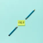 a word idea written on a sticky note placed between broken pencils