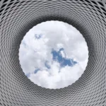 low angle photography of grey and black tunnel overlooking white cloudy and blue sky
