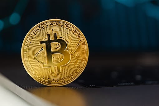 Golden Bitcoin coin standing upright on a laptop keyboard, representing digital currency.