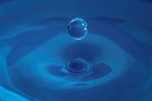 A high-speed capture of a water droplet splashing on a blue background, showcasing fluid dynamics.