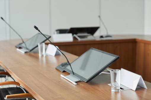 A modern conference room featuring sleek monitors and microphones on a wooden tabletop, perfect for meetings.
