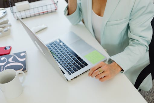 Businesswoman in office attire working on a laptop at a desk, symbolizing modern professional life.