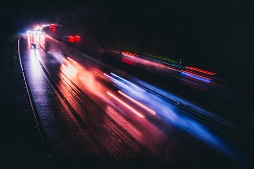 Long exposure photo capturing vibrant light trails on a rainy highway night.