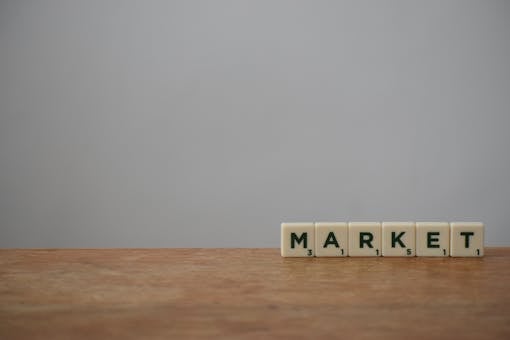 Scrabble tiles spelling 'Market' on a wooden table with a minimalist background.